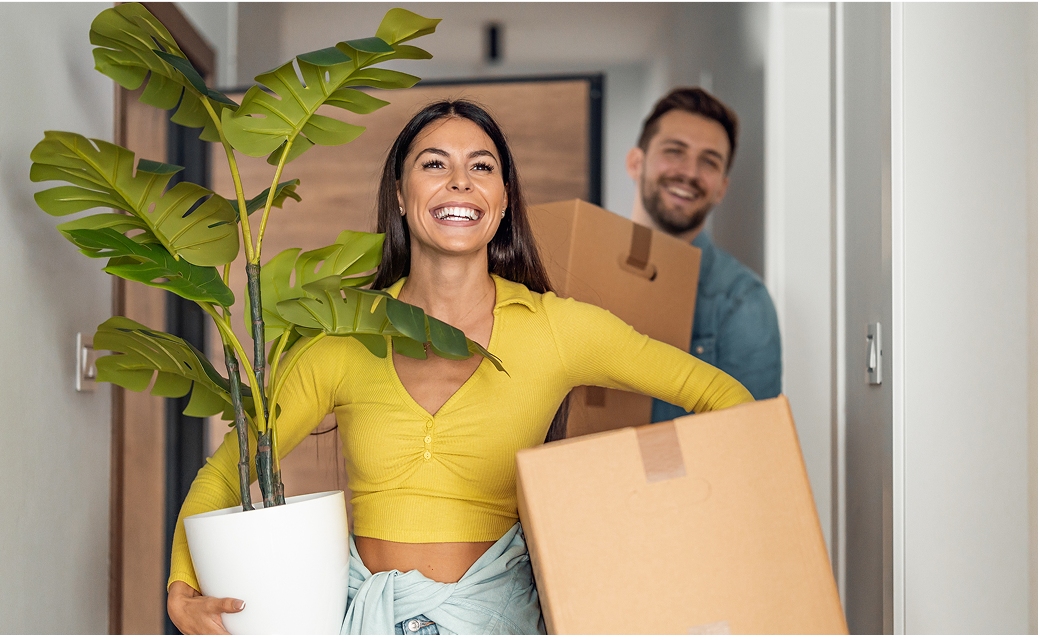 Couple moving into a new place carrying boxes and plants